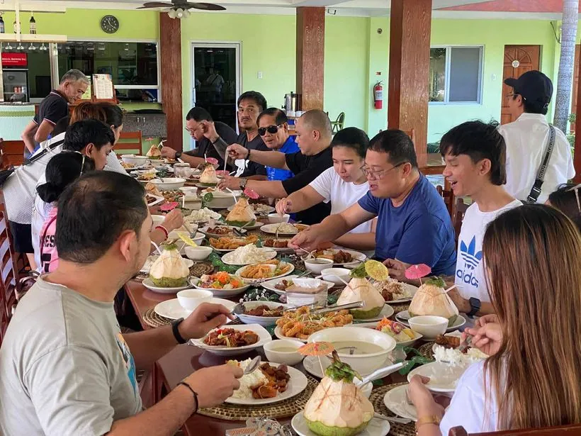 A tour group sharing a long lunch table with fresh coconuts