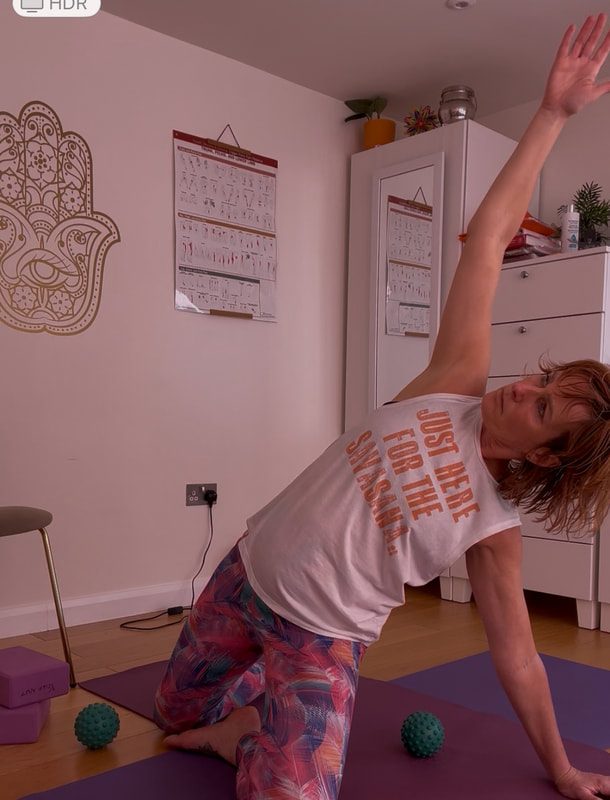 Caroline in a side-bending yoga posture in her studio, one arm reaching overhead