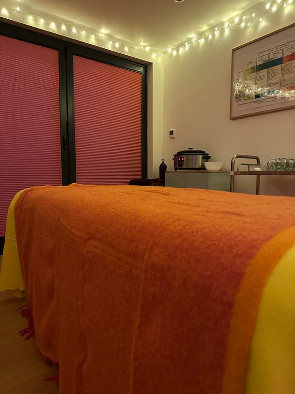 The treatment room at the Laddingford clinic: a massage couch with an orange blanket, soft lights and a pink wall